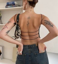 a woman with tattoos on her back standing in front of a bookshelf