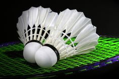 two white badminton balls sitting on top of a green racket