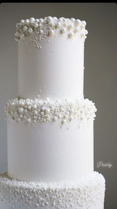 a three tiered white wedding cake with pearls