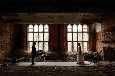 a bride and groom standing in an old building with broken windows on the floor, surrounded by debris