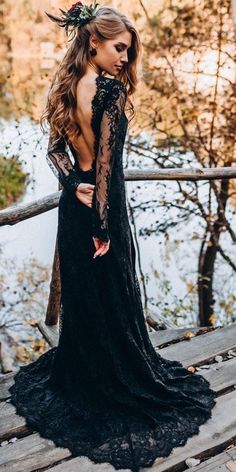 a woman in a black dress standing on a wooden bridge with her back to the camera