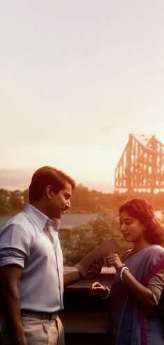 a man and woman standing next to each other in front of a roller coaster at sunset