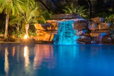 an outdoor pool with waterfall and palm trees in the background at night, lit up by colorful lights