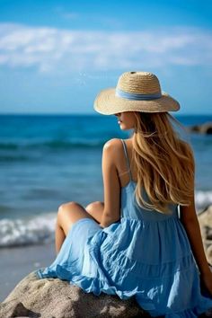 a beautiful woman sitting on top of a rock near the ocean wearing a straw hat