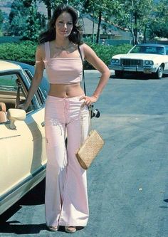 a woman standing in front of a car with her hand on her hip and holding a purse