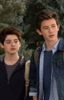 two young men standing next to each other in front of some trees and one is wearing a backpack