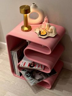 a pink shelf with magazines and vases on it next to a wall mounted lamp