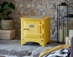 a yellow stove sitting on top of a stone floor next to a potted plant