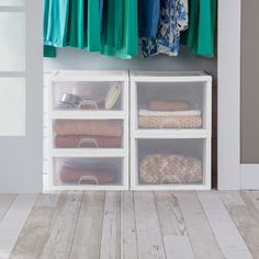 an organized closet with clothes hanging on the rack and plastic bins full of clothing