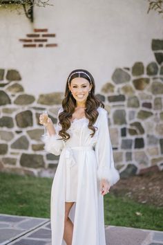 a woman in a white dress and headpiece is standing on the sidewalk with her hand up