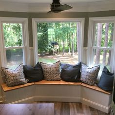 a window seat with pillows on it in front of two windows and a wood floor