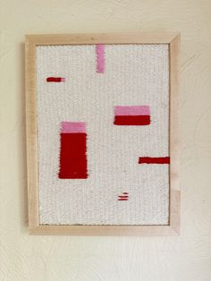 a painting hanging on the wall with red and pink squares painted on it's surface