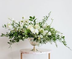 a vase filled with white flowers sitting on top of a marble table next to a wall