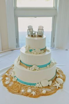 a wedding cake with two chairs on top and sea shells around the bottom, in front of a window