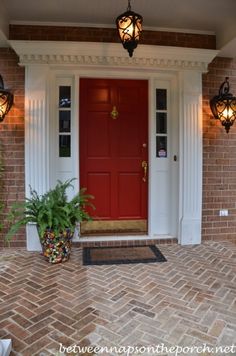 a red front door with white columns and two potted plants