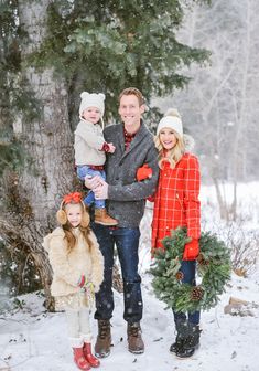 a man, woman and two children are standing in the snow with christmas wreaths