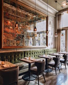 an empty restaurant with green velvet booths and wooden tables in front of a large painting on the wall