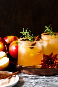 two glasses filled with apple cider next to apples