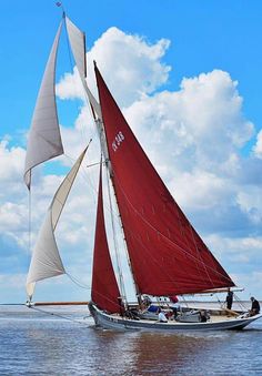 a sailboat with red sails sailing in the ocean under a blue sky filled with clouds