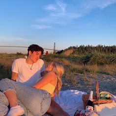 a young man and woman sitting on the ground next to each other in front of a picnic basket