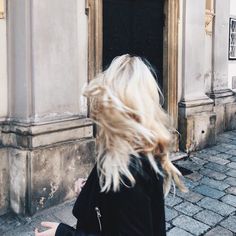 a woman with blonde hair is walking down the street in front of an old building