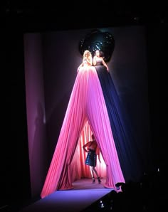 two people standing on top of a pink tent in the middle of a dark room