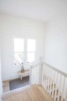 an empty white room with wooden floors and a plant on the table in the corner