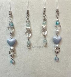 three necklaces with hearts and pearls hanging from chains on a white surface, one has a light blue heart