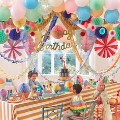 two children sitting at a table in front of a birthday cake with balloons and streamers