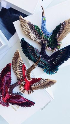 four pairs of bird shaped brooches sitting on top of a white card next to a box