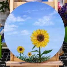 a sunflower painted on the side of a wooden easel with blue sky and clouds in the background