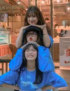 three young women sitting on top of each other in front of a storefront window