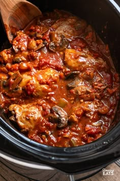 a slow cooker filled with meat and sauce on top of a wooden spoon in the crock pot