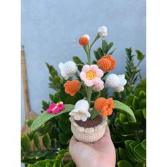 a crocheted flower arrangement is shown in front of a blue wall and green leaves