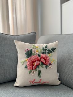 a white pillow with red flowers on it sitting on a gray couch next to a window