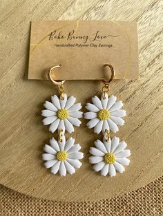 white and yellow daisy earrings with gold accents on a wooden table next to a business card