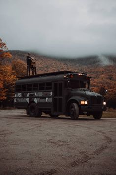 two people standing on top of a black bus