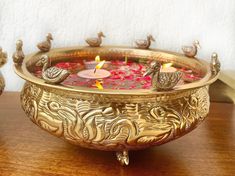 a brass bowl with candles in it on a table next to two figurines