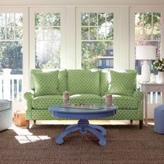 a living room with green couches and blue table in front of two large windows