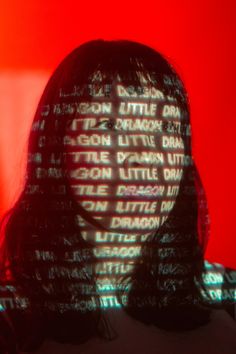 Frontwoman Yukimi of the band Little Dragon standing front of a red backdrop. The Words "Little Dragon" are projected on her face Light Projector Photoshoot, Photo Shoot With Projector, Plexiglass Photoshoot, Prism Photography Portrait, Photography With Projector, Photoshoot With Projector, Pandora Photoshoot, Projecter Photoshoot, Projector Photoshoot Background