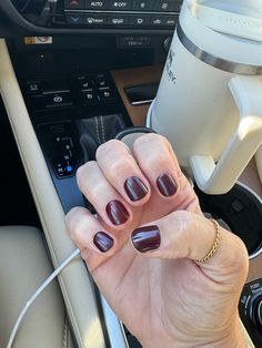 a woman's hand with maroon nail polish holding a coffee cup in her car