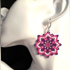 a pair of pink and purple beaded earrings sitting on top of a white mannequin head