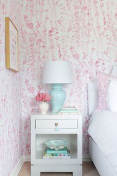 a white nightstand sitting next to a bed in a bedroom under a pink wallpaper