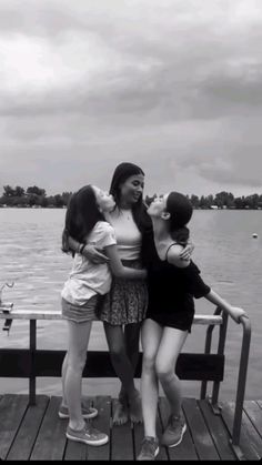 three girls are hugging on a dock by the water and one girl has her arms around another woman's shoulders