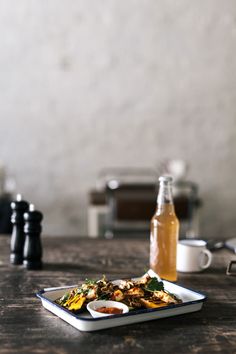 a plate with some food on top of it next to a glass bottle and pepper shaker