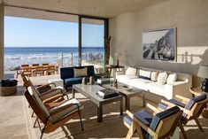 a living room filled with lots of furniture next to an ocean side wall covered in windows