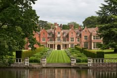 a large brick house sitting on top of a lush green field next to a lake