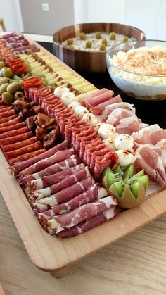 an assortment of meats and cheeses on a wooden platter next to other foods