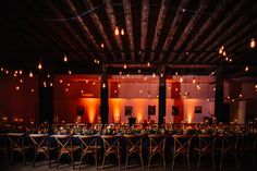 a long table with many chairs and lights hanging from it's ceiling is set up for an event