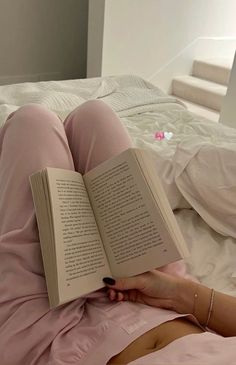 a woman laying in bed with her legs crossed and holding an open book above her head